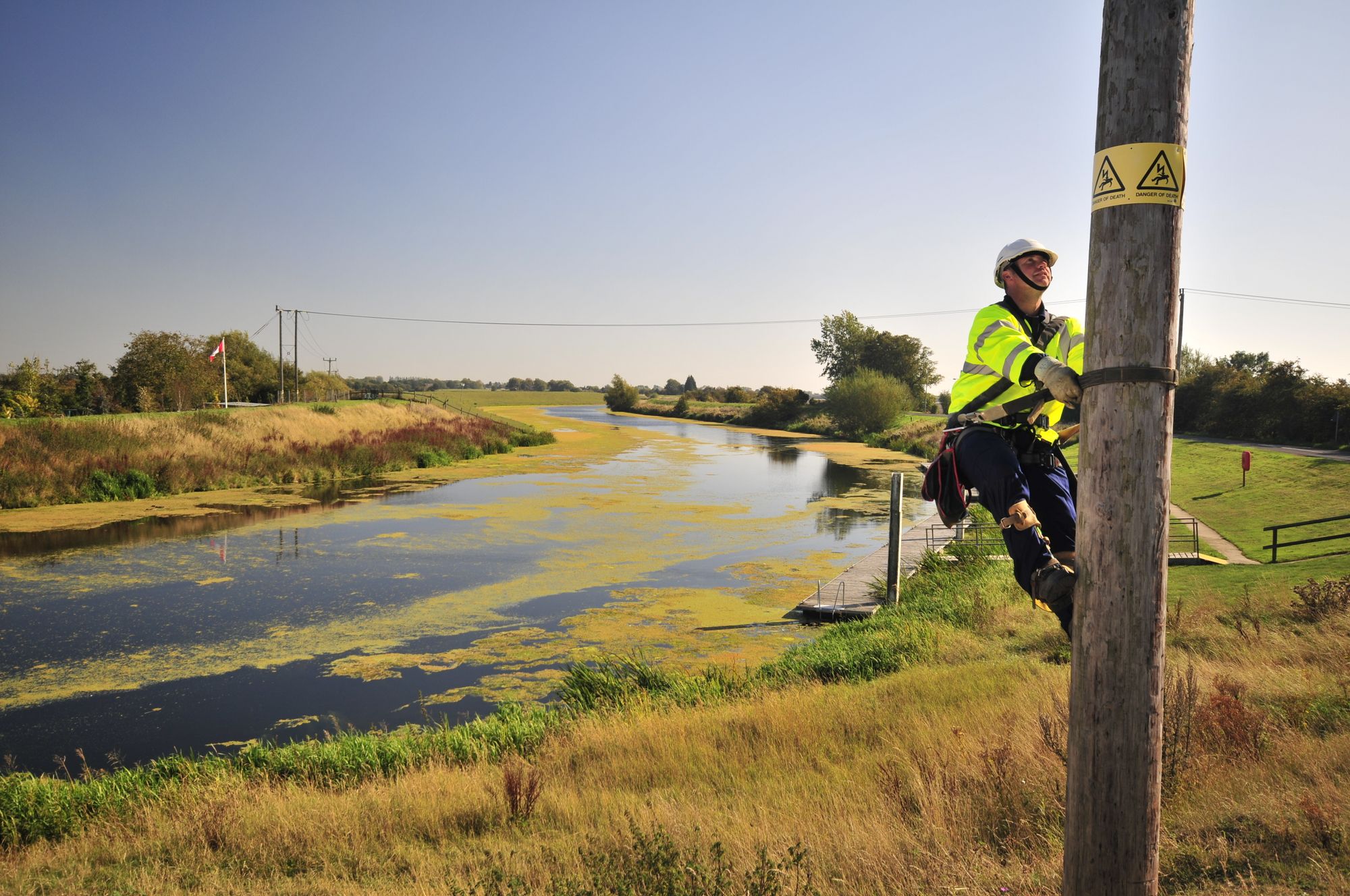 Electrician climbing overhead pole with health and safety gear